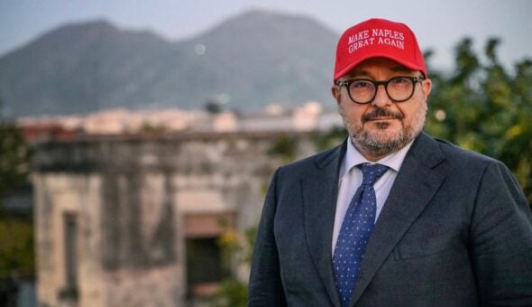 «Make Naples great again»: Sangiuliano lancia il berretto trumpiano. Poi trova al ristorante Angela Merkel e cantano “Funiculì funiculà“